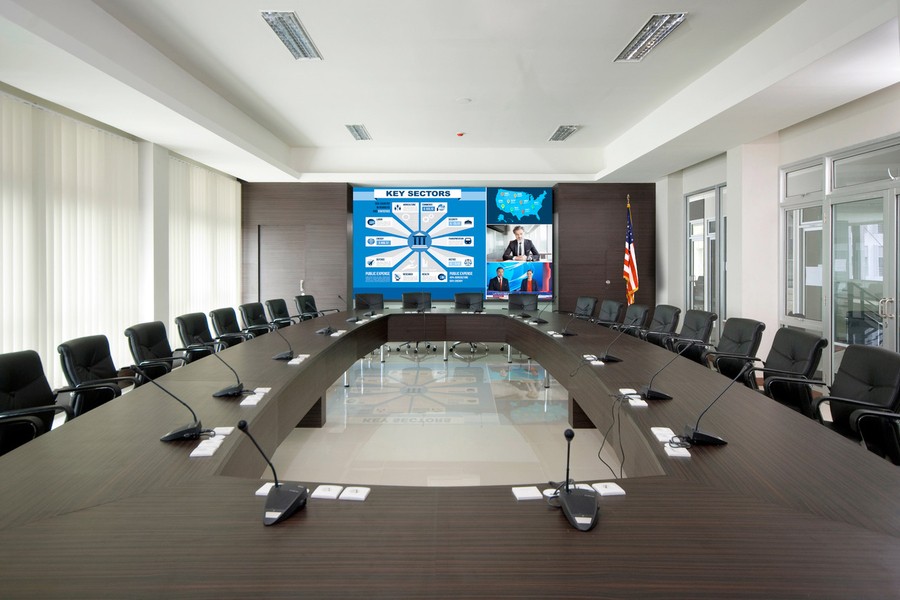 A large conference room with an LED video wall and microphones lining the table.