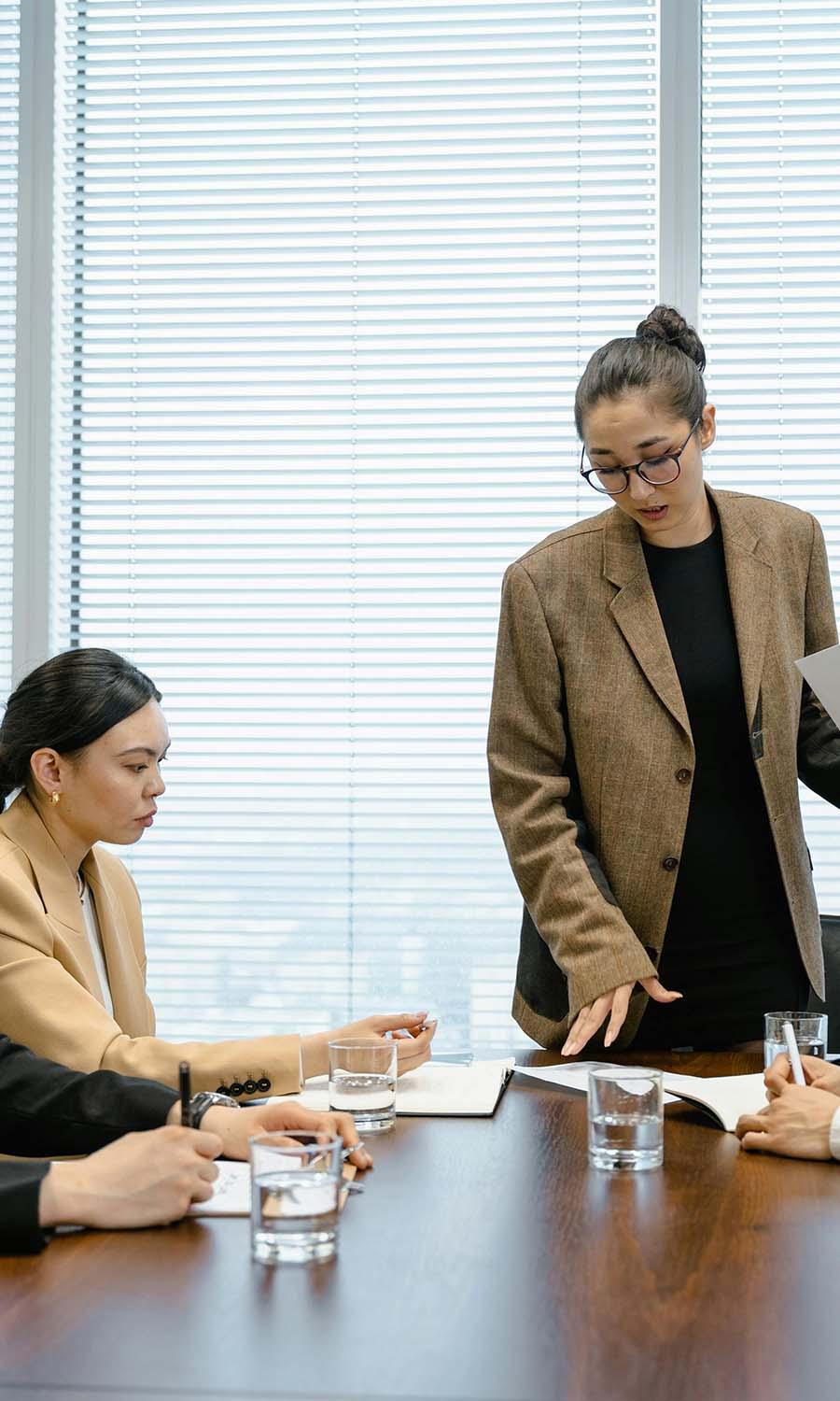 women in a. conference room at a wooden table in front of some windows